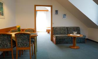 A cozy room with a dining area and a couch. Natural light streams through a window, creating a pleasant atmosphere.