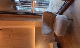 A cozy armchair is in a room with wooden paneling. Large windows offer a view of the outdoors and nature.