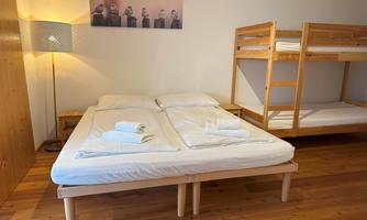 A cozy room with a double bed and a bunk bed. The decor is simple and modern, with a warm wooden floor.