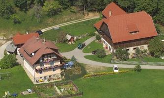 A rural environment with several buildings, including a farmhouse with a red roof and balconies. Surrounded by green meadows and a small garden.