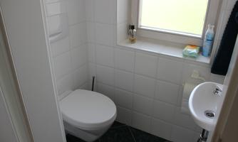 A small, bright bathroom with a toilet and a sink. A window provides natural light.