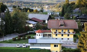 A quiet residential area with several houses, surrounded by trees. In the background is a beautiful view of a landscape with a lake.