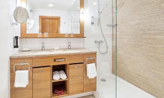 A modern bathroom with a double sink made of wood and a walk-in shower. Fresh towels are placed on the sink.