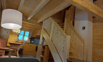 A cozy interior with wooden walls and a wooden staircase. There is a dining area and a warm light from a floor lamp.