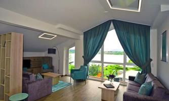 A modern living room with large windows and a view of the landscape. The furnishings include comfortable sofas, a table, and decorative curtains.