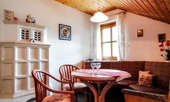 A cozy dining area with a round table and chairs. The wooden ceiling and the windows create a warm ambiance.