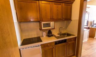A modern kitchen with wooden furniture, a stove, and a microwave. The kitchen setup is functional and well-organized.