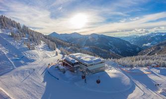 A wintry mountain landscape with plenty of snow and a ski hut. The sun shines over the majestic peaks.