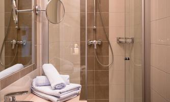 A modern bathroom with a shower, sink, and large mirrors. Clean towels are placed on the shelf.