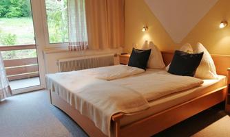 A cozy bedroom with a large double bed and soft pillows. The large windows offer a view of the green landscape outside.