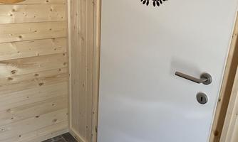 A white door with a sign that says "Sailfish," in a room with light wooden paneling. Next to the door, there is a round mirror.