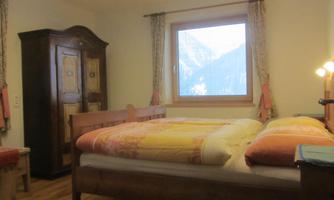 A cozy bedroom with a double bed and a large window that overlooks the mountains. There is also a classic wardrobe and warm colors.