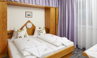 A cozy room with a double bed and wooden cabinets. The windows are decorated with light curtains, and the ambiance is friendly and inviting.