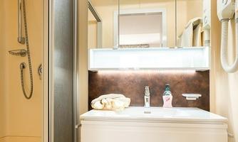 A modern bathroom with a shower, a white sink, and large mirrors. The walls are painted in warm beige tones, creating an inviting atmosphere.