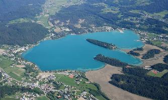 A beautiful lake with clear, blue water, surrounded by green forests and meadows. Nearby are small villages and fields.