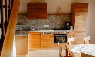 A modern kitchen with wooden cabinets and a marble countertop. The room includes a dining area with a table and chairs.