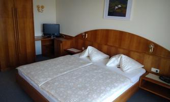 A cozy hotel room with a double bed and a television. The walls are made of light wood, and the room is simply but invitingly furnished.