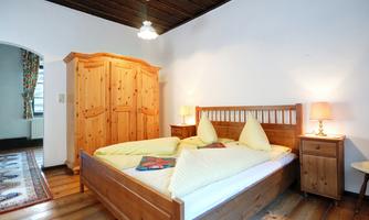 A cozy bedroom with a large wooden bed and two yellow cushions. In the room, there is a wooden wardrobe and nightstands with lamps.