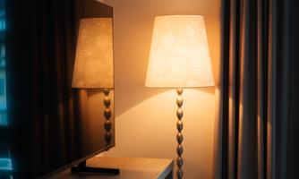 A cozy corner with a television and a floor lamp. The lamp emits warm light and casts a soft shadow on the wall.