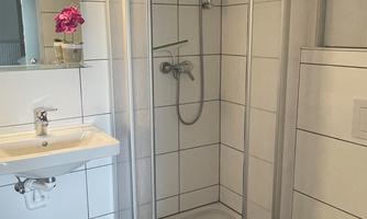 A modern bathroom with a shower in a glass cabin. The sink and the toilet are clean and elegantly designed.