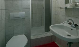 A modern bathroom with bright tiles and a wooden ceiling. It includes a shower, a sink, and a red bath mat.