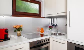 A modern kitchen with white cabinets and a stove. On the countertop, there are flowers and a drink.