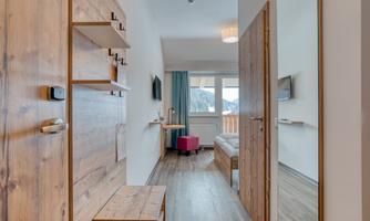 A bright room with wooden furniture and large windows. In the background, there is a cozy seating area with a view.