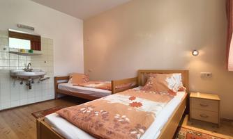 A simple room with two single beds and some decoration. There is a wall with a sink and a small nightstand.