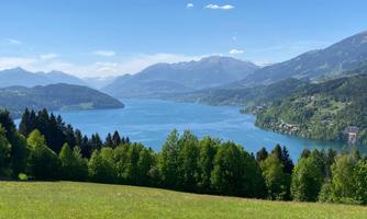 A picturesque lake surrounded by mountains and green forests. The sky is clear and the landscape is very inviting.