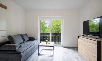 A modern living room with a gray sofa and a low table. Large windows offer a view of green trees.