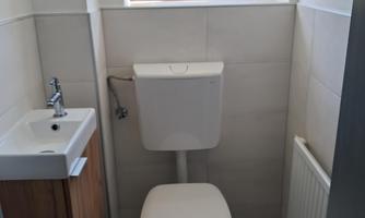 A modern toilet in a small bathroom. There is a window, a hand basin, and a radiator.