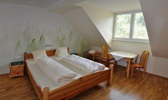 A simple bedroom with two beds and a small table. Large windows let in plenty of daylight.