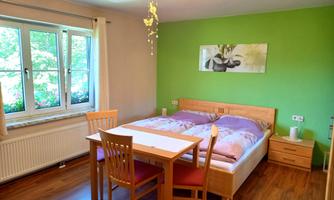 A cozy bedroom with a double bed and a table with chairs. The green wall and the window create a friendly atmosphere.