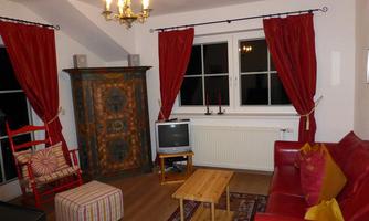 A cozy living room with a red sofa and a wooden coffee table. The windows are decorated with red curtains, and there is an antique cabinet in the room.