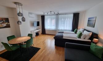 A modern room with two beds, a sofa, and a dining table. Large windows provide plenty of natural light.
