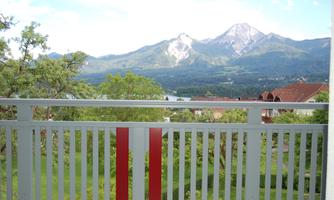 A view from a balcony of green landscapes and majestic mountains. The sky is clear and blue, highlighting the tranquility of the surroundings.