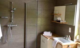 A modern bathroom with a walk-in shower and bright tiles. On the other side is a sink with wooden shelves and fresh towels.