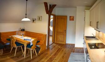 A cozy kitchen with a dining table and chairs. The room has wooden floors and exposed wooden beams.