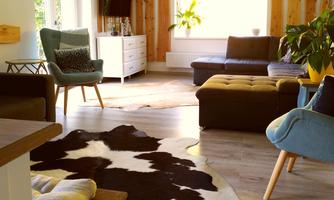 A cozy living space with a dark gray sofa and a light carpet. Large windows let in plenty of light and plants create a fresh atmosphere.