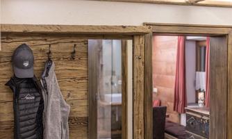 A cozy room with wooden paneling and a view of a bathroom. A jacket and a hat hang on the wall.