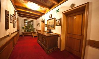 A cozy corridor with wooden details and red carpet flooring. Various pictures hang on the walls, and there is a small console with a plant.