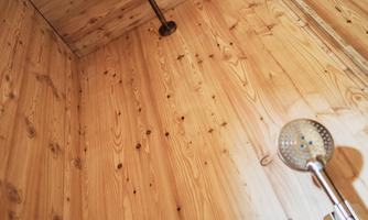 A modern shower with two shower heads in a wooden room. The walls and ceiling are made of wood, creating a natural atmosphere.