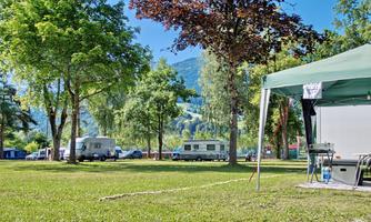 A quiet campsite with green meadows and trees. In the background, mobile homes can be seen, surrounded by beautiful nature.