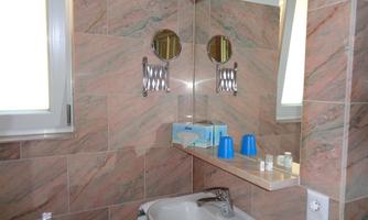 A clean bathroom with marbled walls and a sink. In the background, mirrors and toiletries are visible.