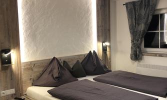 A cozy bedroom with a wooden bed and dark gray bedding. Soft lighting and stylish curtains create a relaxed atmosphere.