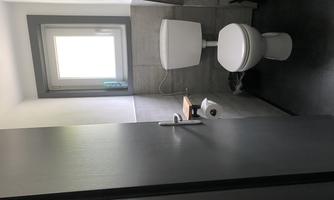 A small bathroom with a toilet and a window. The walls are in neutral colors and the floor is dark.