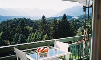 A beautiful balcony with a table and chairs, with fresh fruit on it. In the background, green forests and gentle mountains can be seen.