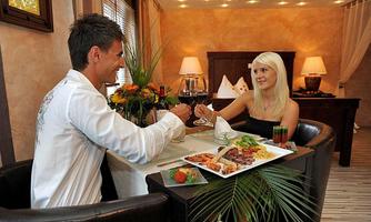 A couple is sitting at a romantic dinner in an elegantly decorated room. On the table lies an assortment of delicious food and drinks.