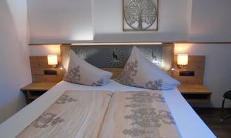 A cozy bedroom with a large bed and decorative pillows. A modern wall decoration and warm light sources hang on the walls.