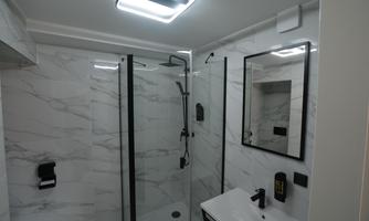 A modern bathroom with a glass shower cabin and marble walls. The large mirror and stylish fixtures create an elegant atmosphere.